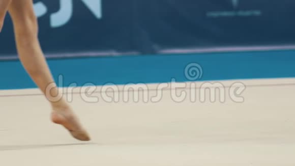 年轻女子在艺术体操比赛中的腿穿着泳装的女孩在舞台上行走并滚动球视频的预览图