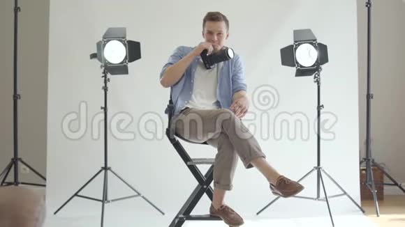 年轻的男摄影师坐在椅子上用相机拍照微笑着看着相机视频的预览图