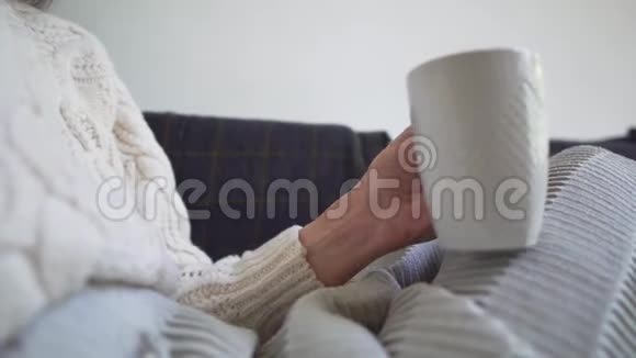特写镜头女孩端着一杯新鲜咖啡藏在毯子里在寒冷的秋日坐在舒适的沙发上视频的预览图