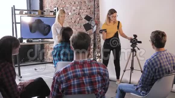 摄影师在专业摄影棚的摄影研讨会上向年轻的创意人士谈论数码单反相机视频的预览图