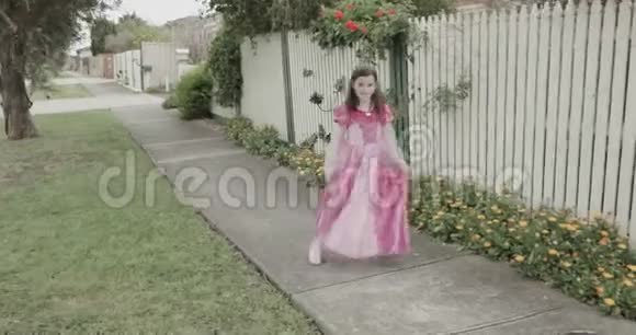 一个穿着公主服装的小女孩在房子外面的篱笆和花前跳舞旋转和旋转视频的预览图