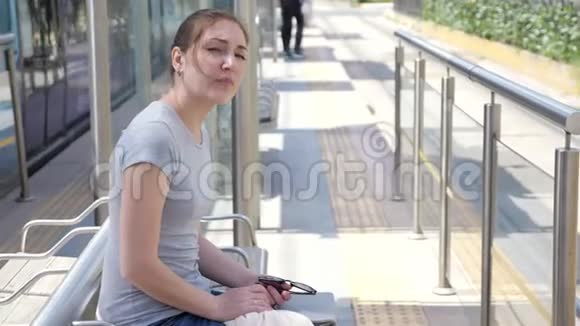 女人坐在长凳上等着晴天电车的到来视频的预览图