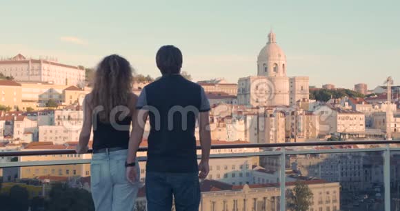 后景一对夫妇拥抱而站在河堤上在清晨的阳光下看着里斯本城视频的预览图