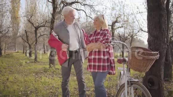 英俊的高白种人白发苍苍的男人在他可爱的妻子身上穿上红色夹克快乐成熟的退休夫妇视频的预览图