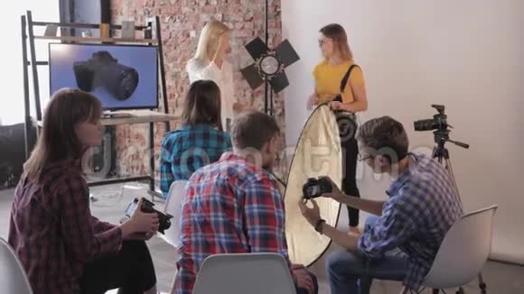 在摄影棚年轻的摄影师教一群有单反相机的人使用摄影棚设备视频的预览图