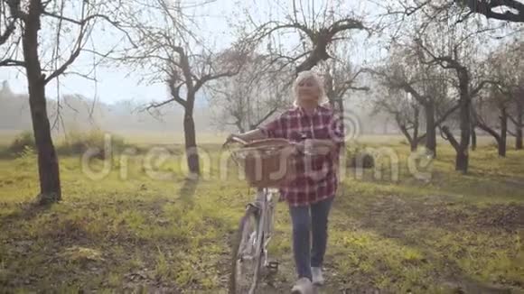 微笑着成熟的白人女人穿着休闲服骑着自行车在雾蒙蒙的公园里散步美丽的欧洲退休女士视频的预览图