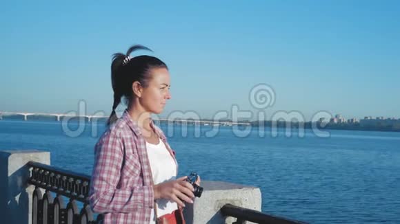 穿着衬衫的女人开着相机快门在河堤上拍照视频的预览图