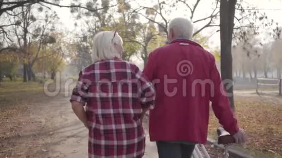 在公园里沿着小巷散步的成熟白人夫妇的后景快乐的退休老人家庭秋天视频的预览图