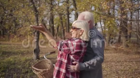 快乐的白种人退休夫妇站在秋林或公园的阳光下微笑成熟家庭的侧观视频的预览图