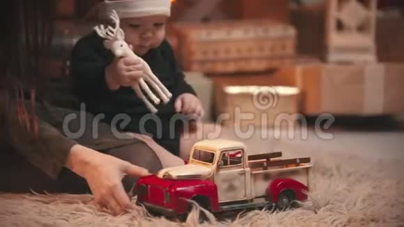 圣诞节概念一个年轻的女人在圣诞工作室和她的小宝宝玩一个抱着玩具鹿和汽车的婴儿视频的预览图