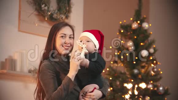 圣诞节概念一个微笑的年轻女子抱着她的小婴儿在圣诞节工作室一个婴儿抱玩具鹿视频的预览图