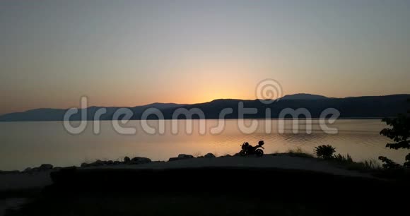 一辆摩托车停在湖岸上夕阳西下五彩缤纷的天空视频的预览图