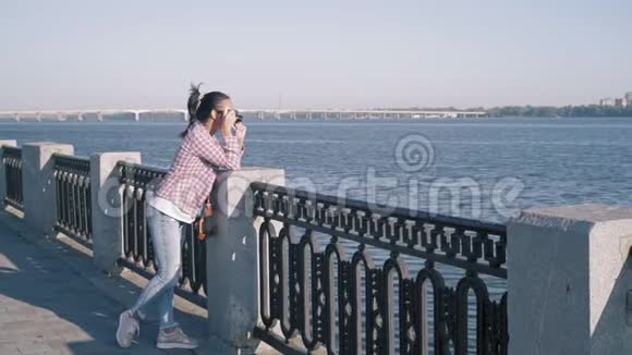 美丽的女人站在河堤上用复古相机拍照视频的预览图