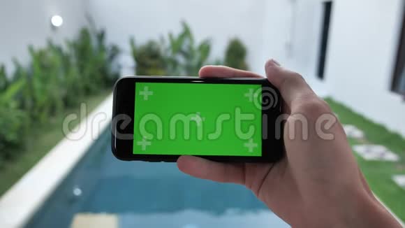 智能手机的特写与绿色屏幕坐在靠近游泳池的家中由人保持水平模式看电影视频的预览图