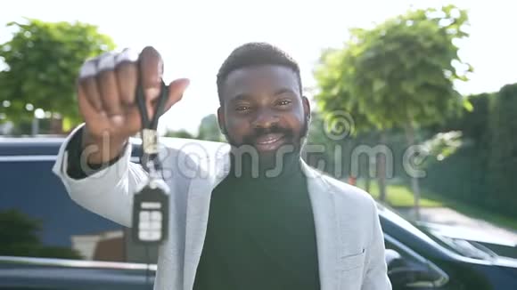 一个满脸胡须的美国黑人男子手里拿着钥匙在他购买汽车的背景上展示着汽车视频的预览图