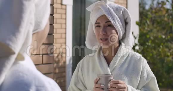 穿着浴袍和发巾的年轻女士站在户外看着相机微笑着的肖像漂亮的女孩视频的预览图