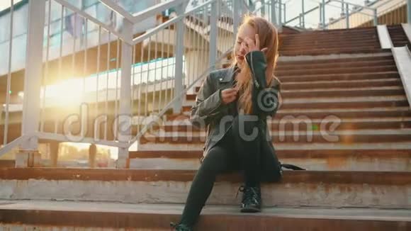 穿黑色皮夹克的孤独女孩坐在阳光背景下的楼梯上穿皮夹克的漂亮女孩视频的预览图