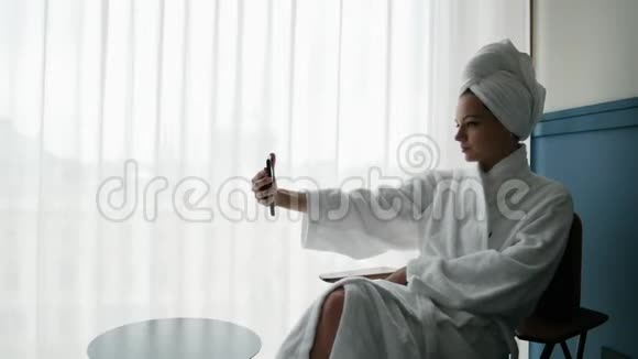 身穿浴袍头上戴毛巾的美女在手机上自拍视频的预览图