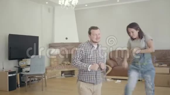 年轻快乐的白人夫妇在客厅里和未包装的家具跳舞住在新房子的幸福家庭视频的预览图