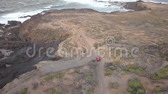 红色的汽车正行驶在尘土飞扬的道路上在海边的悬崖上视频的预览图