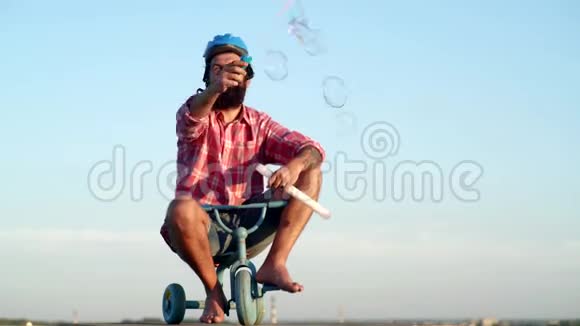 代人和成长阶段带着滑稽脸的嬉皮士在乡间小路上骑着儿童自行车的滑稽男人视频的预览图