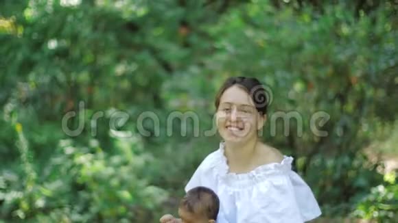 年轻漂亮的母亲在公园里用绿色的树叶背景缓慢地抚养她刚出生的女儿年轻快乐视频的预览图