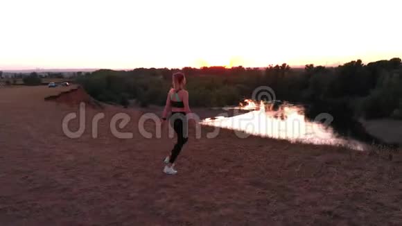一架漂亮的照相机女孩运动员在日落时跑了一圈来到悬崖边双手张开视频的预览图