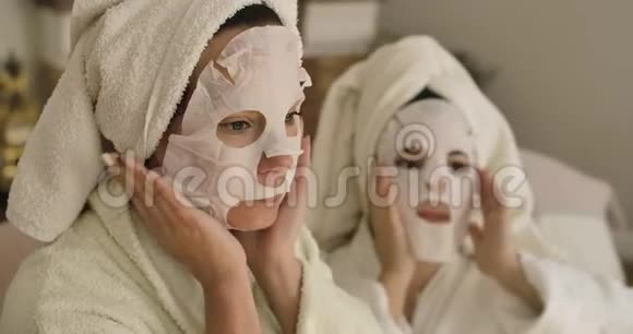 两名戴面罩的白人成年妇女的肖像穿着发巾和浴衣的女孩在家休息视频的预览图