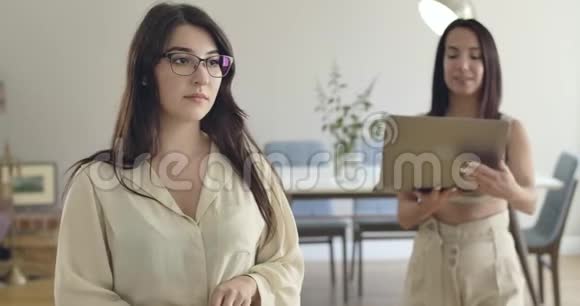 年轻女子来到戴着眼镜和休闲服的白人女孩面前在笔记本电脑屏幕上显示一些东西视频的预览图