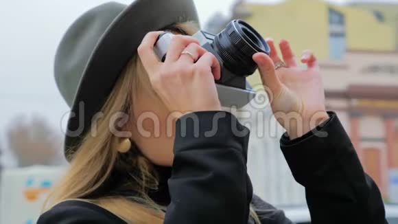一个年轻的高加索女人一个戴着帽子的时髦女郎在一个老式的电影相机上拍照概念记者博客作者视频的预览图