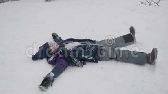 一个年轻的女孩躺在雪地里移动她的胳膊和腿做一个雪天使视频的预览图