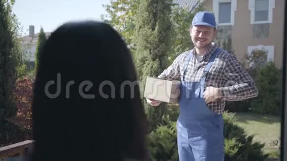微笑白种人男快递员穿着蓝色工作服给女顾客送盒子等待她检查视频的预览图