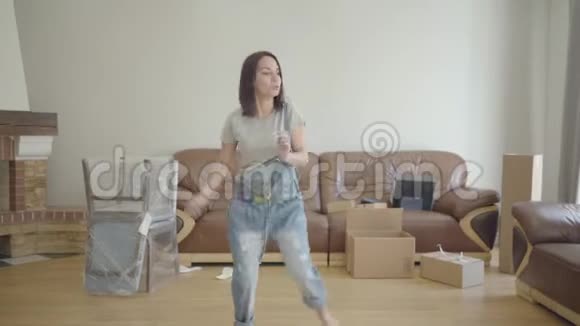 年轻快乐的白人女人在客厅里跳舞带着未包装的家具坐在地板上成年女孩视频的预览图