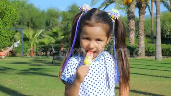 小可爱的女孩吃冰淇淋走在棕榈树旁边的草坪上视频的预览图