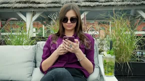 迷人的年轻女性使用手机喝一杯冷的莫吉托鸡尾酒在露台享受美好时光视频的预览图