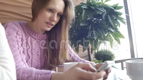 两个漂亮的女朋友在智能手机上的社交媒体上看照片在咖啡馆的咖啡休息时间交谈视频的预览图