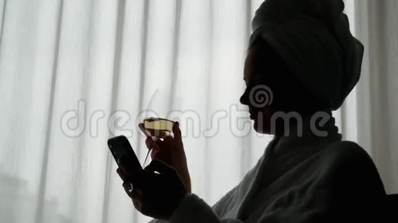 一位身着白色浴袍头上戴着毛巾的优雅女人的特写剪影享受着一杯酒的享受和使用视频的预览图
