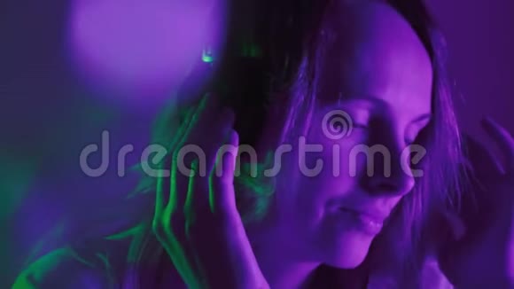 女孩喜欢听耳机上的音乐霓虹灯流畅的节拍和流畅的镜头背景模糊光线视频的预览图