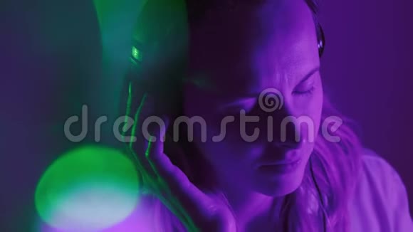 女孩喜欢听耳机上的音乐霓虹灯流畅的节拍和流畅的镜头背景模糊光线视频的预览图