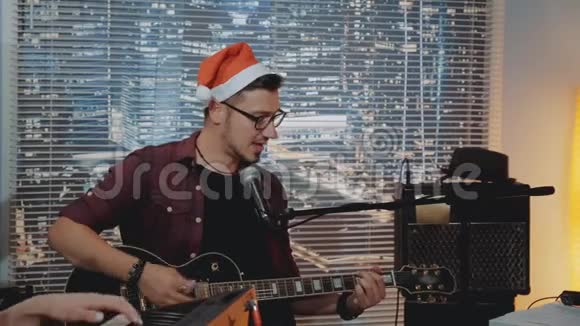 戴着圣诞帽的才华横溢的年轻人在家庭录音室录制他的新曲目视频的预览图