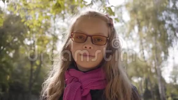 一个十几岁的白人女孩站在秋天公园的阳光下看着相机的肖像微笑的金发女郎视频的预览图
