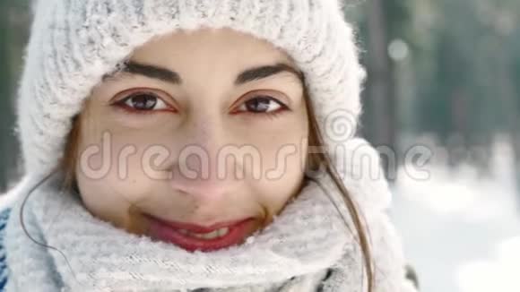 穿着羊毛帽戴着长长的暖围巾的美丽微笑的女子在雪地冬季公园的模糊的极端特写镜头视频的预览图