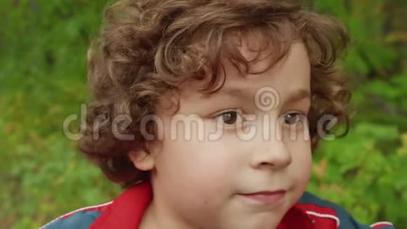 夏天公园的卷发黑发男孩的肖像在绿色公园里骑着自行车闭上脸的少年男孩英俊的男孩视频的预览图