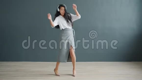 可爱的亚洲女孩在灰色背景的工作室跳舞戴着耳机玩得开心视频的预览图