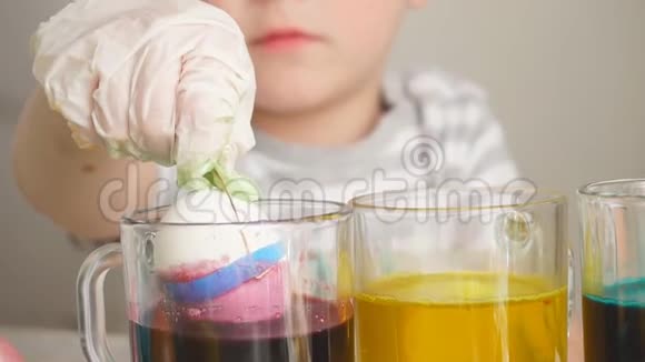 特写孩子用一只手拿着一个鸡蛋把它扔进一杯油漆里视频的预览图