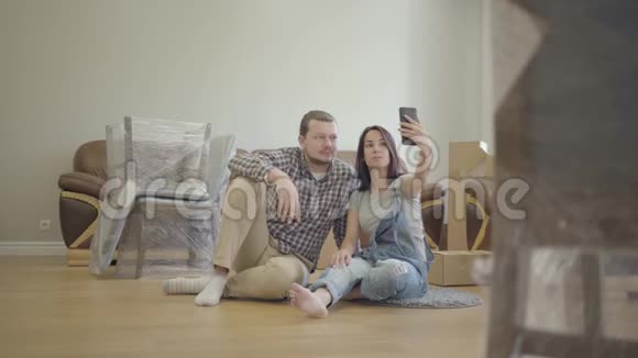 快乐的高加索夫妇自拍就像坐在客厅的地板上带着新的家具微笑的夫妇搬进来视频的预览图