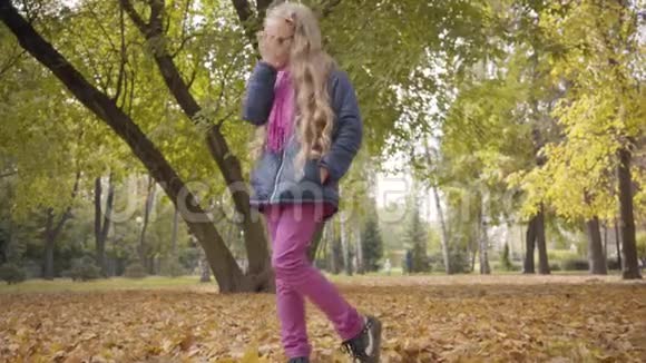 一个可爱的金发白种人少女戴着眼镜站在秋天的公园里对着镜头眨眼的肖像视频的预览图