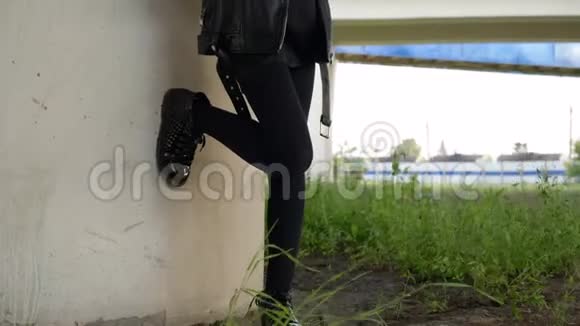 摇滚女孩穿黑色皮夹克使用手机户外在城市的车桥下寻找智能手机的朋克女孩视频的预览图