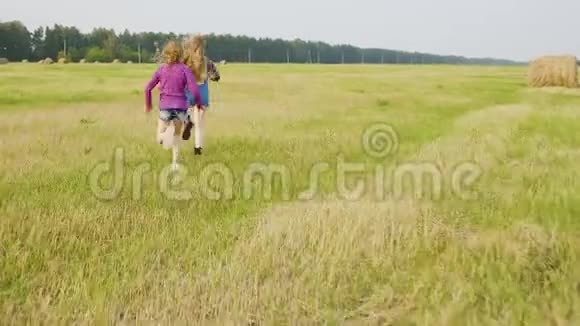 两个十几岁的女孩在干草堆背景下奔跑在乡间田野上可爱的女孩在乡间奔跑视频的预览图