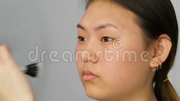 专业化妆师将粉底遮瑕或荧光粉涂在亚洲韩国模特的脸上并用特殊的刷子视频的预览图
